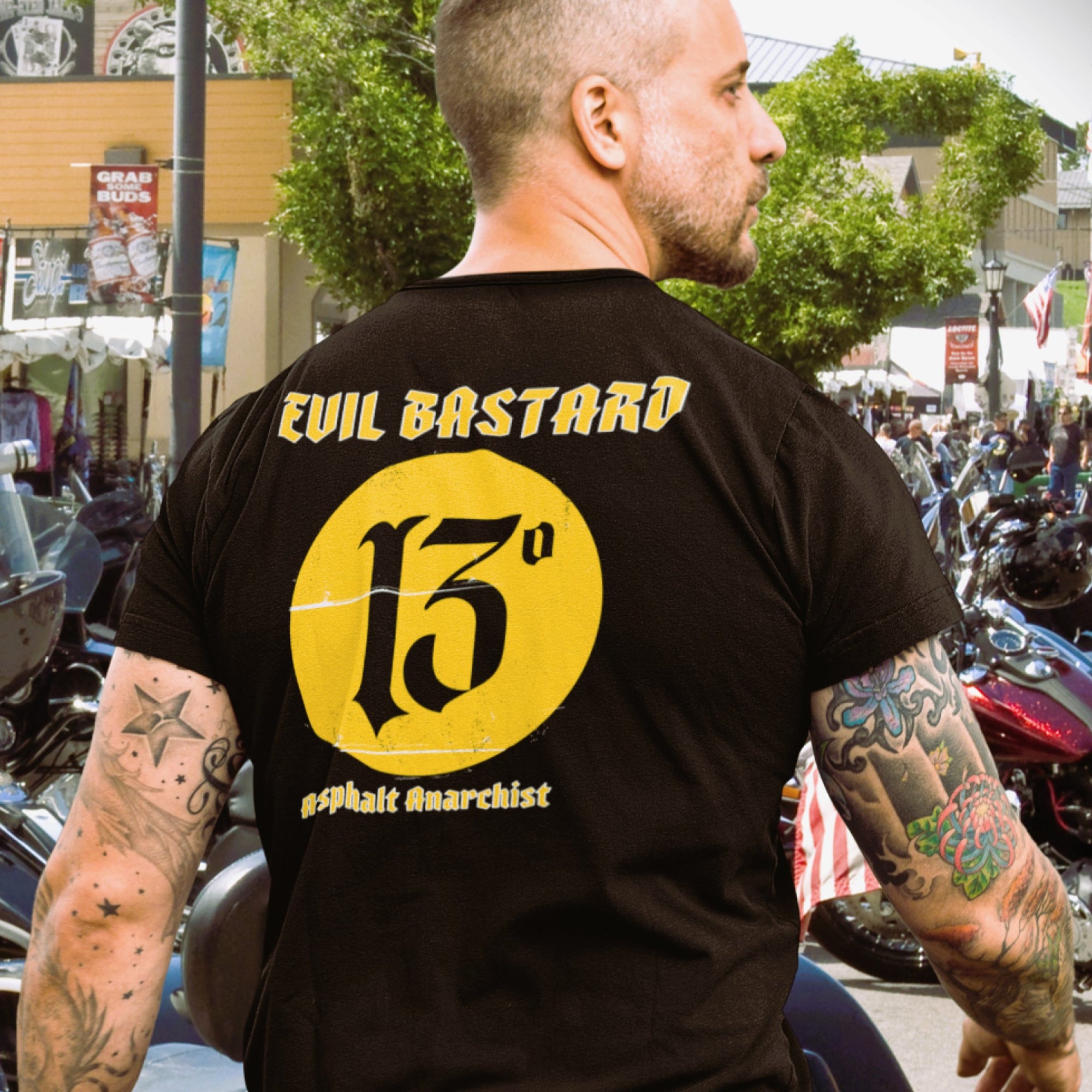 A tatted down biker checks out the crowd at a motorcycle rally. He is wearing the Evil Bastard T-Shirt from Asphalt Anarchist Clothing Co. KUSTOM KULTURE APPAREL & PRODUCTS - Fuck the Status Quo