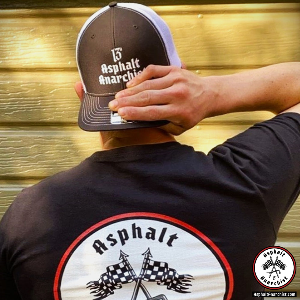 
                  
                    A young man stands facing his garage. He is wearing the Asphalt 13 Trucker Hat & Classic Red Line T-Shirt from Asphalt Anarchist Clothing Co. KUSTOM KULTURE APPAREL & PRODUCTS
                  
                